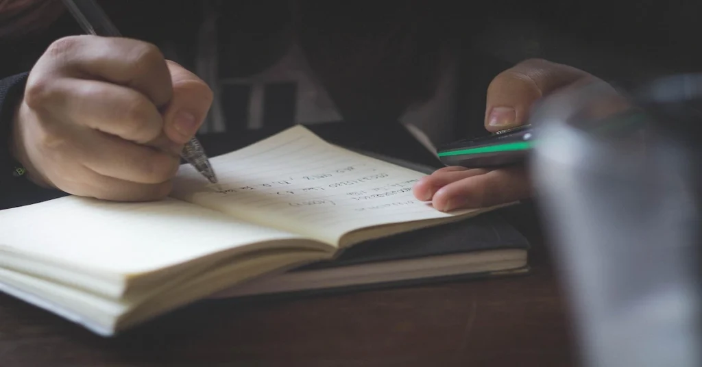 student taking handwritten notes on paper next to a laptop, comparing digital notes and paper notes